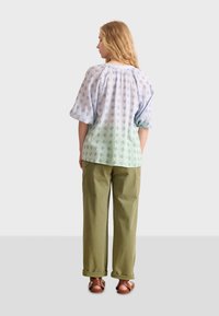 Blusa azul claro con estampado y mangas abullonadas, dobladillo degradado, combinada con pantalones sueltos de color oliva. Las sandalias tienen un diseño de tiras cruzadas.