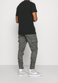 Svart kortärmad t-shirt kombinerad med grå cargobyxor med rutigt mönster och siddragkedjor, bärs med grå högskorna.