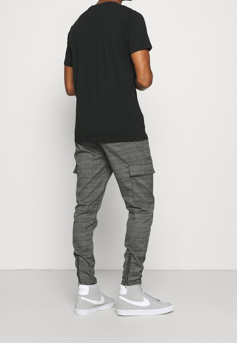 Svart kortärmad t-shirt kombinerad med grå cargobyxor med rutigt mönster och siddragkedjor, bärs med grå högskorna.