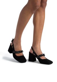 Tacchi slingback neri con punta quadrata, realizzati in suede, con tacco grosso e una comoda cinghia decorativa a catena.