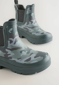 Zelené camo gumové gumáky s elastickými bočnými panelmi, textúrovanou podrážkou a spevnenou špičkou pre zvýšenú odolnosť.