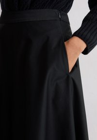 Jupe noire au textile lisse, avec une taille ajustée, des poches latérales et un ourlet fluide. Détail zippé au dos.