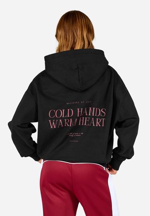 Black hooded sweatshirt with pink text on the back, featuring the phrase "COLD HANDS WARM HEART." Material appears soft with a relaxed fit.