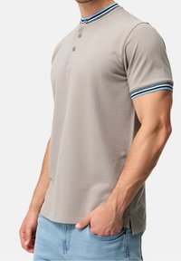 Jasnoszary polo z krótkim rękawem, z niebieskimi i białymi paskami, trzema guzikami z przodu, fakturowana tkanina, delikatne logo marki na piersi.