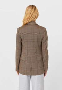 Bruine blazer met hondentandruit, getailleerde pasvorm, inkeping revers en lange mouwen. Soepele textuur met een gestructureerd silhouet.
