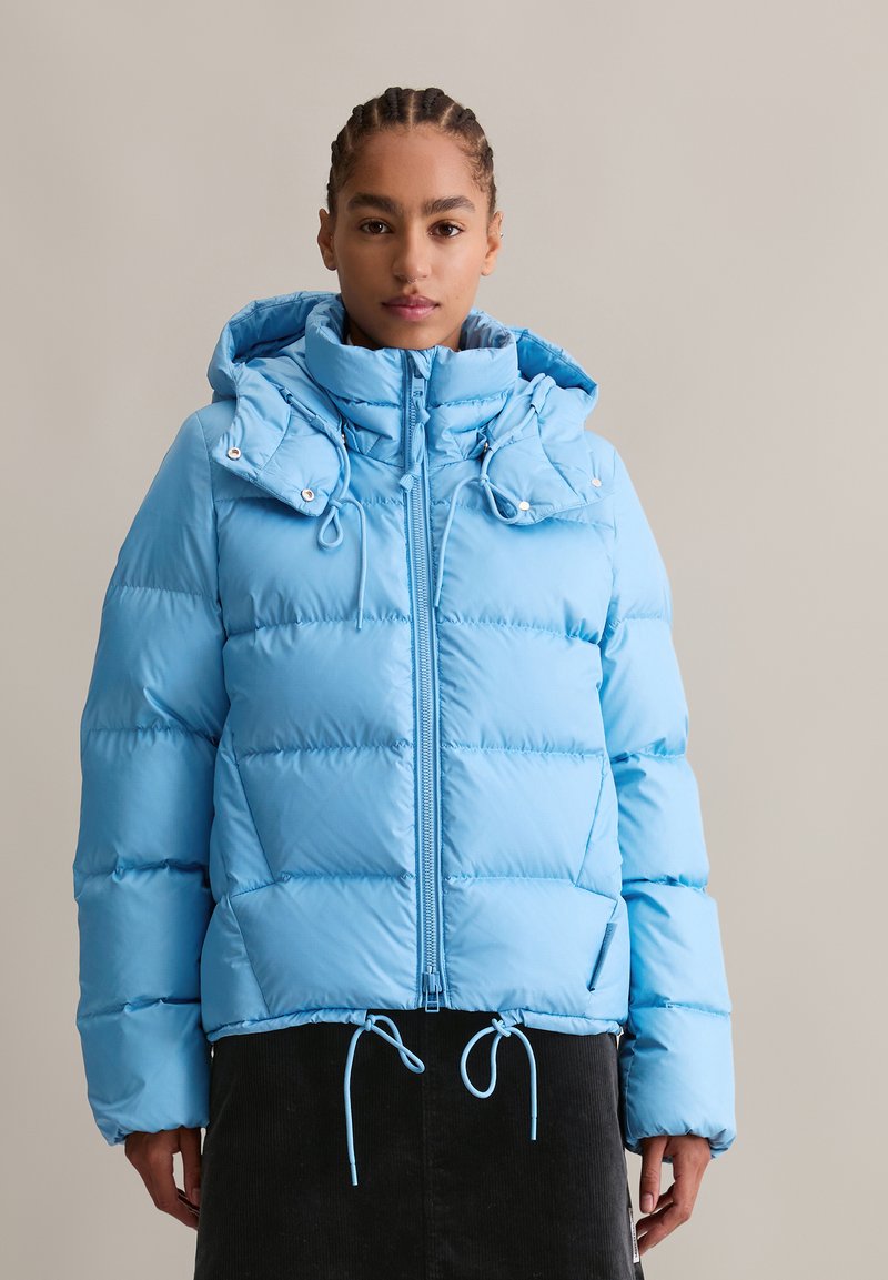 Hellblaue Steppjacke mit einem Reißverschluss vorne, verstellbarer Kapuze und Kordelzugsaum. Mit unterteilten Steppabschnitten und Taschen an den Seiten.