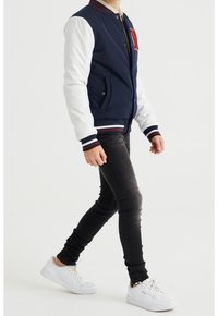 Laivaston pommikilkka, jossa on valkoiset hihat, ribbed-kaulus ja raidalliset hihansuut. Varustettu taskuilla ja punaisella emblemillä rinnassa. Yhdistetty mustiin skinny-farkkuihin ja valkoisiin lenkkareihin.