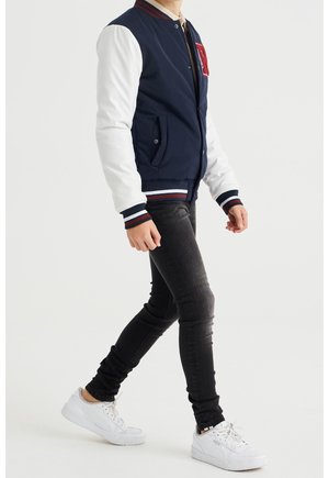 Laivaston pommikilkka, jossa on valkoiset hihat, ribbed-kaulus ja raidalliset hihansuut. Varustettu taskuilla ja punaisella emblemillä rinnassa. Yhdistetty mustiin skinny-farkkuihin ja valkoisiin lenkkareihin.