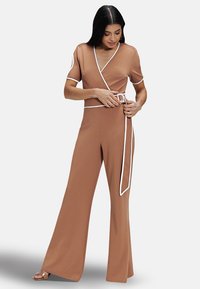 Brown wrap-style jumpsuit with short sleeves, white trim accents, and a belted waist. Flared pants create a flowy silhouette.