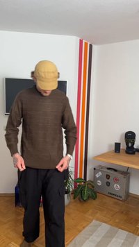 Brown knitted sweater with a textured pattern, paired with loose black cargo pants. A beige cap completes the outfit.