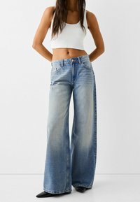 Hellblaue, weite Jeans aus Denim mit einem verwaschenen Finish. Sie besitzen eine hohe Taille, ein Fünf-Taschen-Design und einen Knopfverschluss.