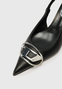 Pantof cu tocul înalt din piele neagră, cu vârful ascuțit, având un accent cu cataramă argintie în față și un design slingback. Textură netedă.