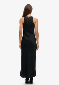 Robe en satin noir longue avec un design ajusté et un dos décolleté. Comprend une fermeture éclair au dos et une texture lisse et fluide.