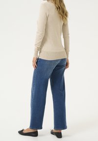 Pull beige à manches longues avec ourlet côtelé, associé à un jean bleu ample et des ballerines noires, mettant en valeur une coupe décontractée.