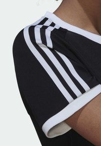 Svart träningsskjorta med vita accenter. Har tre vertikala vita ränder på axeln, ribbad vit krage och en slät textur.