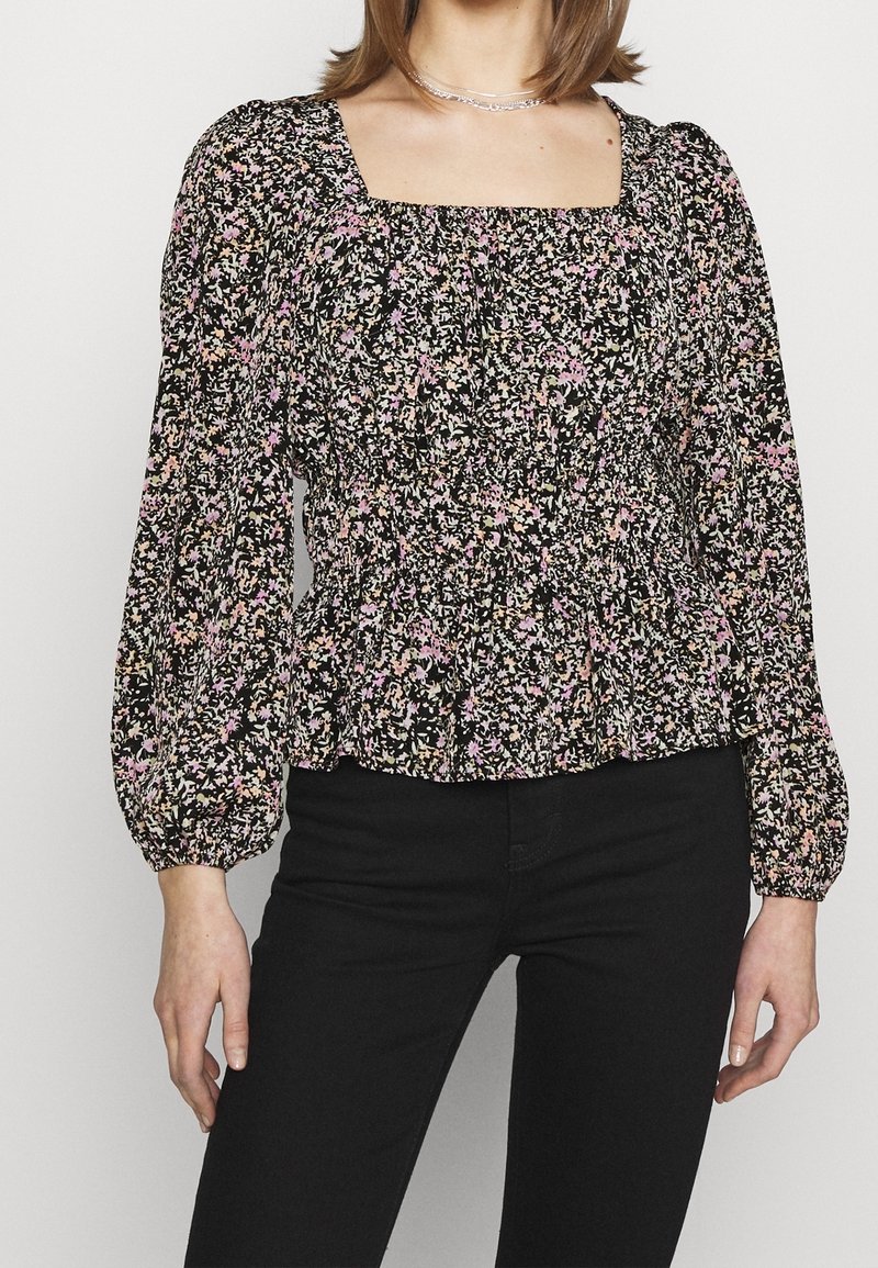 Svart blommig långärmad blus med fyrkantig halsringning, smockad midja och livliga rosa och gula blommönster på en mörk bakgrund.