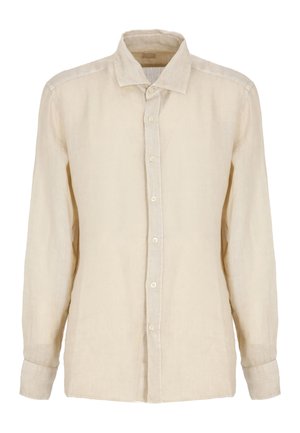 Uomo che indossa una camicia beige a maniche lunghe con bottoni e pantaloncini abbinati, con scarpe marroni senza lacci, in piedi su sfondo bianco.