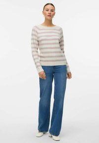Maglione a righe in rosa chiaro e crema, con scollatura ampia e maniche lunghe, abbinato a jeans a trombetta blu e scarpe bianche.