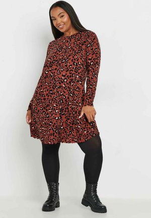 Braun gepunktetes Kleid mit langen Ärmeln, einem ausgestellten Rock und gewelltem Saum, kombiniert mit schwarzen Leggings und Schnürstiefeln.