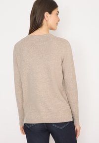 Beżowy sweter dzianinowy z okrągłym dekoltem, długimi rękawami i prążkowanymi mankietami, charakteryzujący się lekko luźnym krojem i miękką fakturą.
