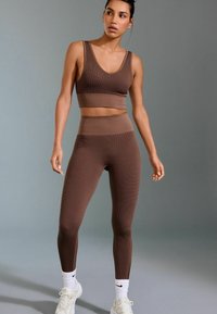 Brown ribbed sports bra and high-waisted leggings set. Smooth texture, minimalist design, featuring a wide waistband and fitted shape.