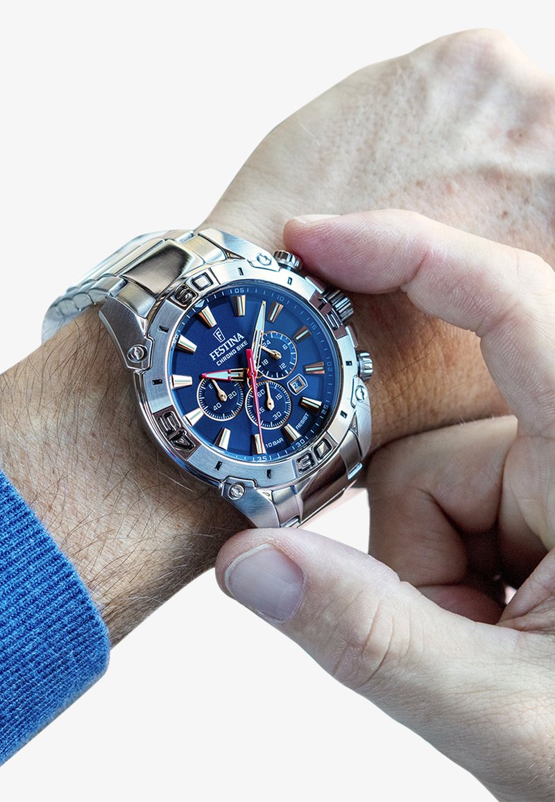 Montre en acier inoxydable argenté avec un cadran bleu, fonctionnalités de chronographe, aiguilles lumineuses et un bracelet texturé, en cours d'ajustement sur un poignet.