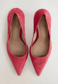 Décolleté in suede rosso con punta affilata, caratterizzati da una superficie liscia, un collo del piede basso e un soletta comoda. Marchio dorato visibile all'interno.