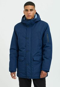 Navy blue padded jacket with a hood, featuring two front pockets, a side zip pocket, and snap button closures. Smooth fabric texture.