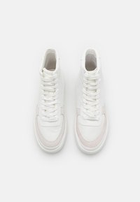 Des baskets montantes en cuir blanc et en daim avec fermeture à lacets, présentant une texture lisse et un patch logo subtil sur la languette.