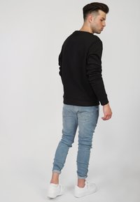 Czarna bluza z długim rękawem, okrągłym dekoltem i dopasowanym krojem. Noszona z jasnoniebieskimi, zwężającymi się dżinsami i białymi trampkami. Prosty design, bez wzorów.