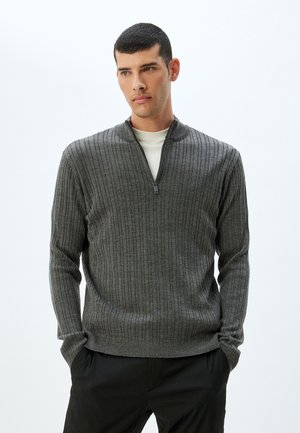 Suéter gris acanalado con un cuello medio con cremallera, mangas largas y un diseño ajustado. La tela tiene una apariencia texturizada y un acabado suave.