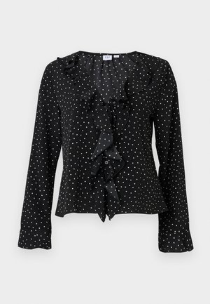 Black long-sleeve blouse with white polka dots, ruffled front detailing, and a v-neck collar from the brand GAP.