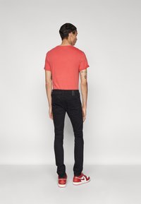 Camiseta roja de manga corta, jeans negros y zapatillas rojas. El conjunto presenta un diseño ajustado con una textura contrastante en la camiseta.