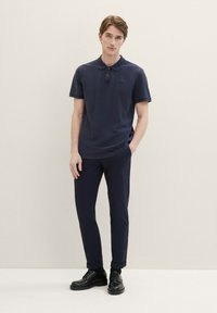 Námornícky modré polokošele s krátkymi rukávmi a trojícou gombíkov, skombinované s námornícky modrými slim-fit nohavicami a čiernymi šnurovacími topánkami.