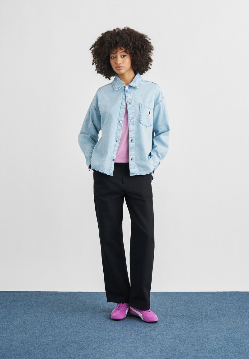 Light blue denim jacket with a chest pocket, worn over a pink top. Black wide-leg pants and bright pink sneakers complete the look.