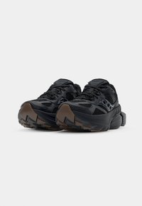 Scarpe da corsa nere in rete con una parte superiore testurizzata, dettagli riflettenti e una suola in gomma marrone spessa con un motivo di battistrada irregolare.