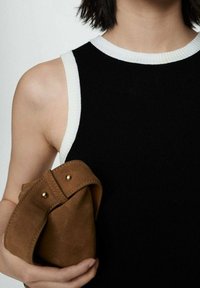 Top de tip cămașă fără mâneci, cu dungă neagră și garnitură albă, asociat cu o poșetă din suedă maro, cu detalii din aur și un design cu clapetă pliată.