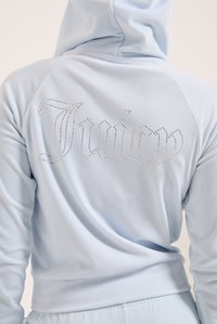 Svetlomodrá mikina s kapucňou z mäkkého materiálu, s dizajnom na chrbte s kamienkovým nápisom "Juicy" v kurzívnom písme.