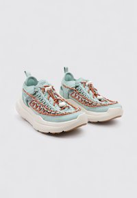 Zapatillas azul claro con cordones trenzados en naranja y blanco, parte superior de cuero texturizado y suela gruesa beige. Lengüeta en el talón.