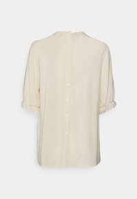 Krämfärgad blus med korta puffärmar med elastiska detaljer, rundad halsringning och en fullständig knapplist på baksidan. Slät textur.