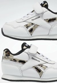 Baskets blanches Reebok avec un accent léopard noir et métallique, dotées d'une bride Velcro, de lacets et d'une semelle en caoutchouc.