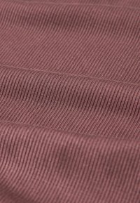 Ribbede stoffer i en dæmpet mauve farve, med smalle, jævnt fordelte ribber. Teksturen fremstår blød og let elastisk.