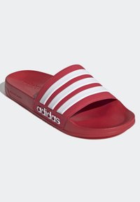 Röda slidesandaler med en strukturerad matt yta, som har tre vita ränder och adidas-logotypen på sidan. Platt såldesign.