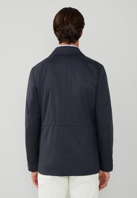 Chaqueta ligera azul marino con cuello entallado, mangas largas y dobladillo redondeado, elaborada en un material sintético suave y con una cintura ajustada.
