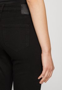 Černé džíny z denimu s přiléhavým střihem, které mají zadní kapsu se šitým obrysem a koženou značkovou nášivkou na pase.