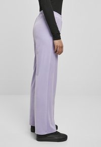 Lavendel wijd-uitlopende broek gemaakt van zacht materiaal met een elastische tailleband. G gedragen met een zwarte lange mouwtop en zwarte sneakers.