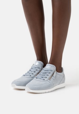 Sneakers in suede grigio chiaro con una superficie texturizzata, lacci frontali, dettaglio con cerniera laterale e suola in gomma bianca.