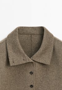 Brown wool coat collar with two black buttons and buttonholes on a plain white background.