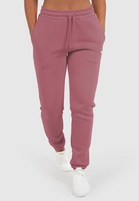 Pantalones deportivos rosas con cintura ajustable, que cuentan con bolsillos laterales y puños en los tobillos, fabricados con una tela suave. Se llevan con zapatillas blancas.