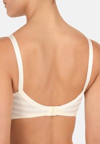 Reggiseno color crema chiaro realizzato in tessuto a righe con chiusura a gancetto e occhiello sul retro. Texture morbida e spalline sottili regolabili.